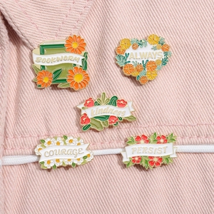 Detailed view of five floral enamel pins with motivational quotes pinned on denim fabric