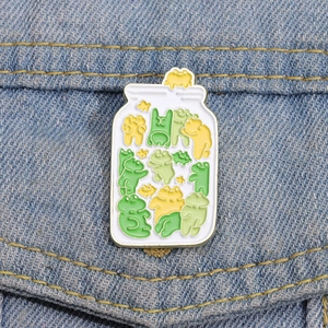 Close-up of a cute enamel frog jar pin attached to blue denim fabric showing fine details