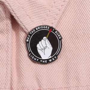 Detail of round enamel brooch with 'May the bridges I burn light the way' text and hand icon