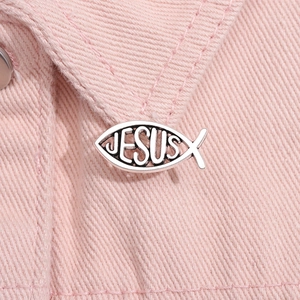 Close-up of silver fish brooch with Jesus engraving on pink denim jacket fabric