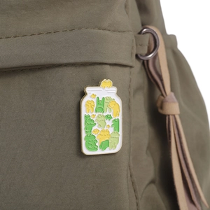 Close-up of a cute frog jar enamel pin attached to a green fabric backpack strap