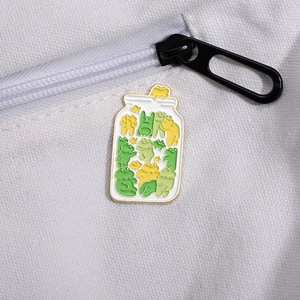 Detailed close-up of a cute enamel frog jar pin attached to a white canvas fabric