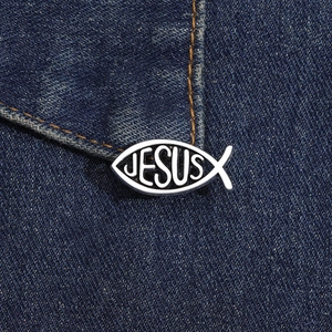 Macro detail of silver Jesus fish brooch badge on dark denim fabric texture