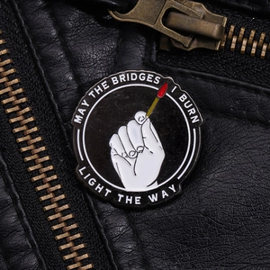 Close-up of May The Bridges I Burn Light The Way enamel pin on a black leather jacket