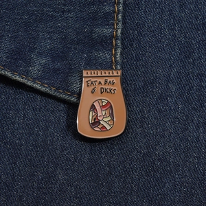 Dettaglio di una spilla in smalto a forma di sacchetto di carta su tessuto denim