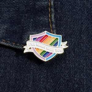 Close-up of rainbow shield enamel pin with I'LL WALK WITH YOU text on denim fabric