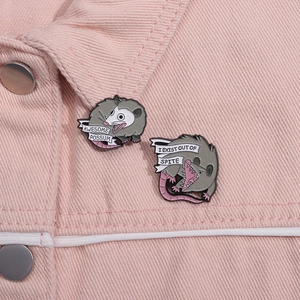 Macro view of cartoon opossum enamel pins with funny quotes on pink denim fabric