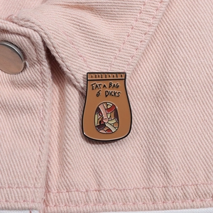 Dettaglio di una divertente spilla smaltata marrone con testo su tessuto denim rosa