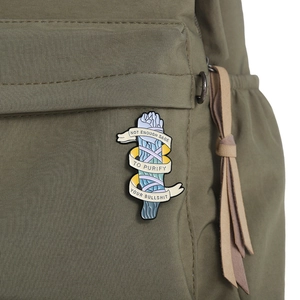 Macro shot of an enamel sage bundle brooch pinned to an olive green backpack fabric