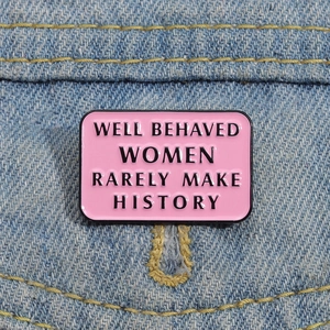 Macro shot of pink enamel badge with quote Well Behaved Women Rarely Make History on denim