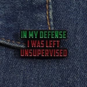 Macro shot of In My Defense enamel pin on denim showing funny red and green letters