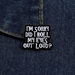 Detail of I'M SORRY enamel pin on denim fabric with funny quote and black finish