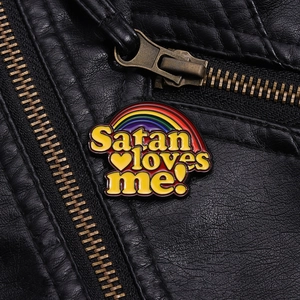Makroaufnahme von Emaille-Anstecker mit Regenbogen und Satan loves me Text auf Lederjacke