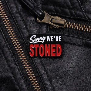 Detail of Sorry We're Stoned enamel pin on a black leather biker jacket texture