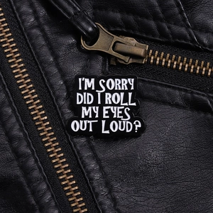 Detail of black enamel pin with I'M SORRY white text on black leather jacket