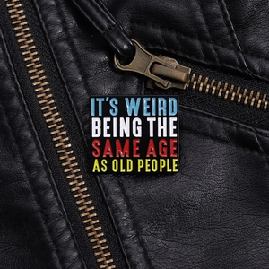 Macro detail of square enamel pin on black leather jacket with humorous text