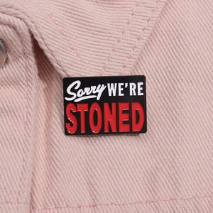 Macro detail of Sorry We Are Stoned enamel pin on pink denim jacket material