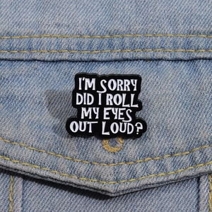 Detail of I'M SORRY enamel pin with humorous text on blue denim jacket material