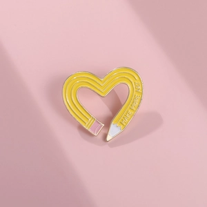 Close-up of heart-shaped yellow pencil enamel pin featuring Make More Art engraving