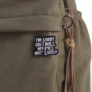 Detail of black enamel pin with white text on olive canvas bag with leather drawstring