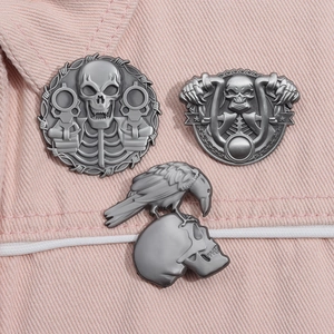 Detail view of gothic skull and raven metal brooches on pink denim fabric texture