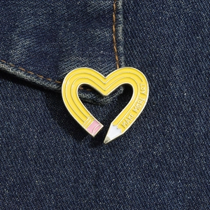 Detail of yellow pencil heart enamel pin with Make More Art text on denim pocket