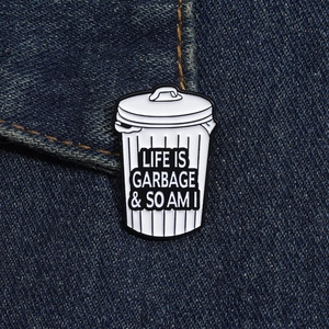 Close-up of funny garbage can enamel pin with humor text on blue denim fabric