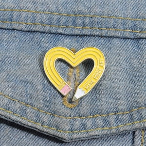 Detail of yellow heart pencil enamel pin with Make More Art text on denim jacket