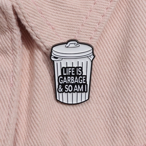 Macro shot of trash can enamel pin with Life Is Garbage text on pink denim fabric