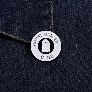 Macro di una spilla smaltata Ghost Hunter Club applicata su tessuto di jeans
