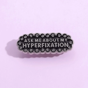 Retro black enamel brooch with Ask Me About My Hyperfixation lettering and silver frame