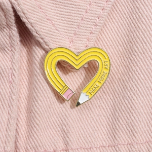 Detailed macro view of heart-shaped yellow pencil enamel pin with Make More Art text