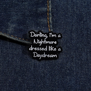 Détail d'un pin's en émail noir avec texte blanc sur un tissu en denim bleu