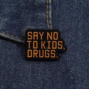 Macro detail of enamel brooch with funny quote pinned on blue denim fabric texture