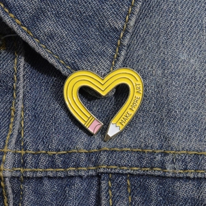 Detail of cute yellow heart-shaped pencil enamel pin on blue denim fabric