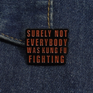 Detail of funny enamel pin on denim with red text Surely Not Everybody Was Kung Fu Fighting