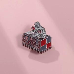 Close-up of DJ Knight enamel pin with 'Tis But A Scratch' text on pink background