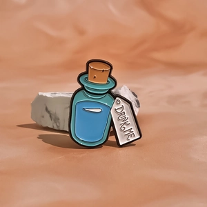 Detail of teal Drink Me potion bottle enamel pin with cork stopper on stone