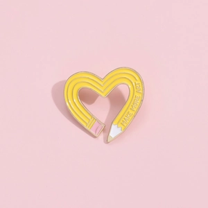 Heart-shaped yellow pencil enamel pin with 'MAKE MORE ART' slogan on a pink background
