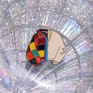 Macro shot of an enamel pin featuring a colorful patchwork cardigan with stars