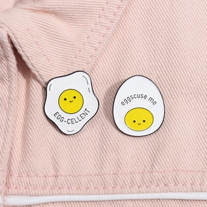 Detail of cartoon enamel pins with 'EGG-CELLENT' and 'eggscuse me' puns on pink denim fabric