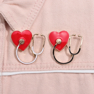 Close-up of heart stethoscope alloy brooches in red and gold on pink denim fabric