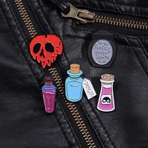 Detail of gothic enamel pins with 'DRINK ME' and skull designs on a black leather jacket
