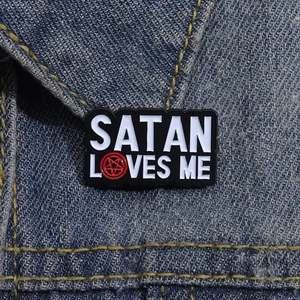 Enamel pin with Satan Loves Me text and red pentagram on blue denim fabric