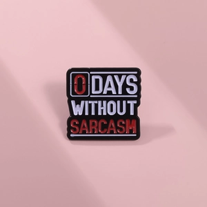 Macro shot of 0 DAYS WITHOUT SARCASM black enamel pin with metal texture and bold red text