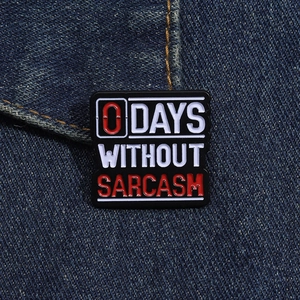 Macro shot of 0 Days Without Sarcasm enamel pin on dark blue denim fabric background