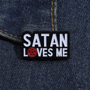 Detail of Satan Loves Me enamel pin with pentagram on denim jacket fabric background