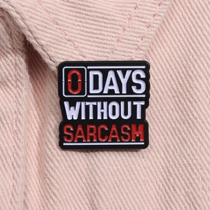 Close-up of square metal enamel pin featuring 0 DAYS WITHOUT SARCASM text on pink fabric