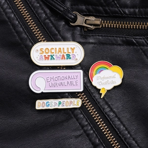 Enamel pins with witty phrases like Socially Awkward on a black leather jacket