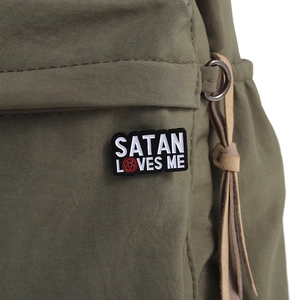 Macro shot of Satan Loves Me enamel pin with red pentagram detail on a green canvas bag